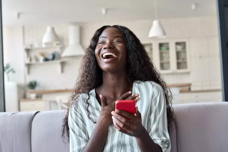 paragraphs for her black african woman laughing on sofa reading text message